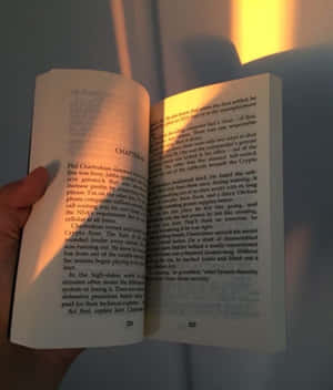 一隻手拿著一本打開的書，帶有可讀的文字和頁碼。 — Apple Watch 壁紙