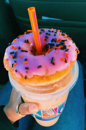 手拿著一杯飲料，上面放著粉紅色糖霜甜甜圈和糖針。 — Dunkin Donuts 壁紙