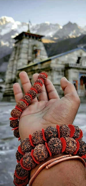 手拿著 Rudraksha 珠子，背後有寺廟和雪山。 — iPhone 16 壁紙