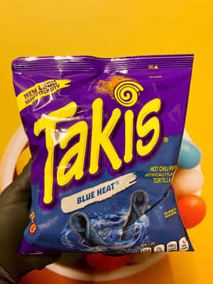 手拿著一袋Takis Blue Heat零食玉米片，背景是黃色。 — 2048x2732 壁紙