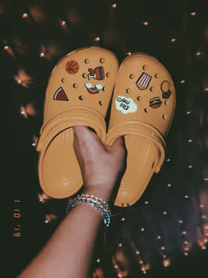 手拿著裝飾有食物和運動貼片的米色Crocs，在仙女燈下。 — iPad Pro 13 壁紙