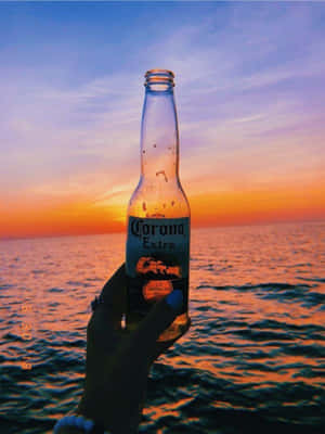 手在海洋日落時拿著Corona啤酒瓶。 — 3:4 壁紙