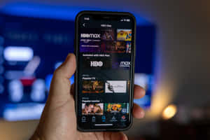 手拿著手機，顯示HBO Max串流應用程式，帶有電視節目和電影。 — HBO 壁紙