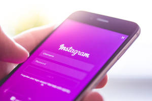 手拿著手機，顯示Instagram登入畫面，背景為紫色。 — 標誌 壁紙