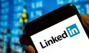 手拿著手機顯示LinkedIn應用程式，背後有股票市場數據。 — 領英 壁紙