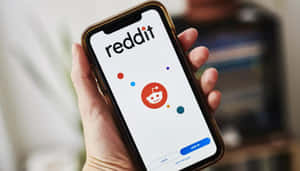 手拿著手機，顯示Reddit應用程式的登入畫面，帶有外星人吉祥物。 — 低調 壁紙