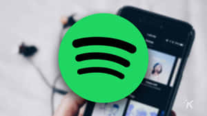 手拿著手機，Spotify應用程式打開，綠色標誌疊加。 — Spotify 壁紙