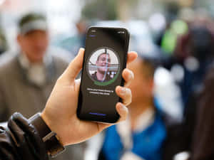 手拿著手機，顯示人臉辨識設定畫面，展示微笑的男士和指示。 — iPhone 鎖定畫面 壁紙