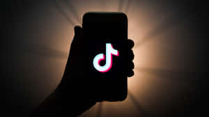 手拿著手機，TikTok標誌在背景光線下發光。 — TikTok 動圖 壁紙