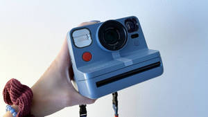 手腕戴著栗色髮圈的手拿著藍色Polaroid相機。