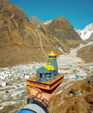 手裡拿著一個小寺廟模型，俯瞰著山村和白雪覆蓋的山峰。 — 廟宇 壁紙