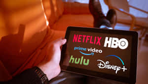 在沙發上手持帶有串流應用程式的平板電腦 — HBO 壁紙