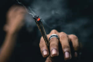 手拿著點燃的大麻煙，煙霧在昏暗光線中升起。 — 抽菸 壁紙