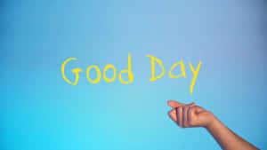 手指指向藍色牆上以黃色寫成的「Good Day」。 — 祝你有美好的一天 壁紙