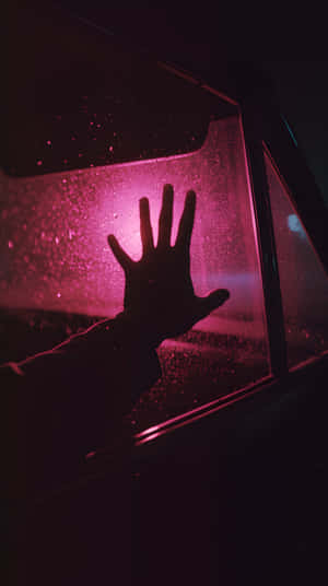一隻手按在雨中的窗戶上，被粉紅色光照亮。 — 1440x2560 壁紙