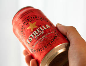 手拿著一個有冷凝水的冰涼紅色Estrella Damm啤酒罐。 — 啤酒 壁紙