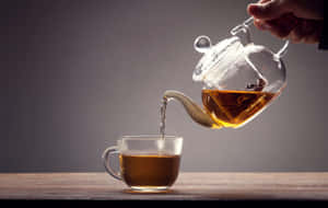 手將琥珀色茶從玻璃茶壺倒入透明杯中，木桌。 — 茶 壁紙
