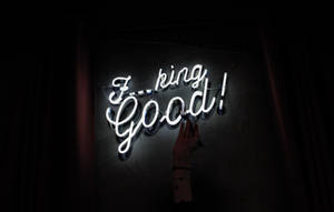 一隻手輕輕觸摸一個明亮的白色霓虹燈牌，上面寫著「F*ing Good!」，在昏暗的房間裡。 — 霓虹美學 壁紙