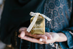 雙手展示一個帶有白色絲帶的金色Eid Mubarak禮物盒。 — 慶祝 壁紙