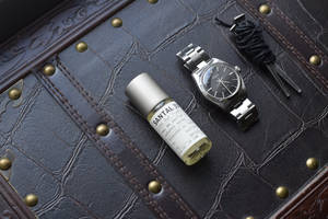 銀色手錶和 Santal 33 香水瓶放在帶黃銅鉚釘的深色皮革上。 — 手錶 GIF 壁紙