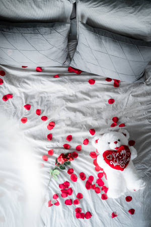 白色泰迪熊拿著心形，上面寫著「Be my Valentine」，在床上與玫瑰花瓣。 — 可愛情人節 壁紙
