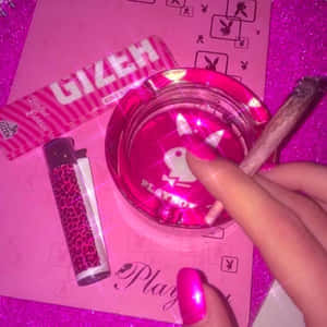 手在粉紅色Playboy煙灰缸上拿著鈍器，配有豹紋打火機和GIZEH紙。 — 花花公子 GIF 壁紙