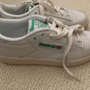 米色地毯上的白色 Reebok Classic 運動鞋，帶有綠色點綴。 — 銳步 壁紙