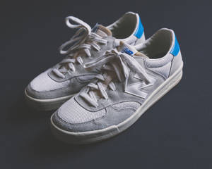 灰色 New Balance 運動鞋，帶有藍色點綴和白色鞋帶，背景為深灰色。