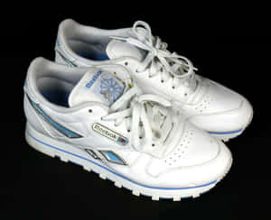 白色Reebok Classic運動鞋，帶有藍色和銀色細節，背景為黑色。 — 銳步 壁紙
