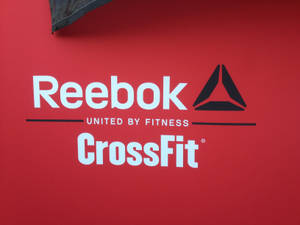 紅色牆壁帶有Reebok和CrossFit標誌及文字「因健身而團結」。 — 銳步 壁紙