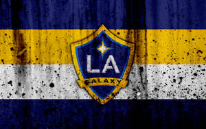 LA Galaxy足球隊標誌，背景為骯髒的藍色、黃色和白色條紋。 — 運動 壁紙