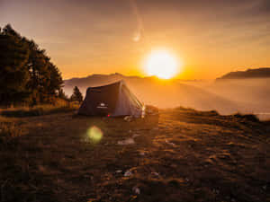 日出時在山脊上搭建的帳篷，背景有霧氣繚繞的山峰。 — 日落 壁紙