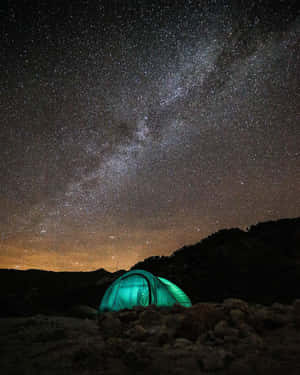 在星空夜空下，一頂發光的綠色帳篷，銀河清晰可見。 — 光線 壁紙