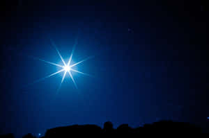 一顆帶有星爆射線的明亮星星，在繁星點點的夜空下照耀著岩石地形。 — 星星 壁紙