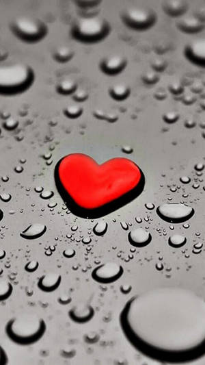 水滴濕潤的銀色表面上的紅色心臟。 — 紅色美學 iPhone 壁紙