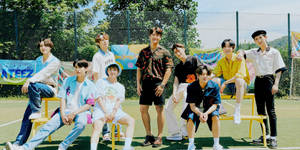 七位K-pop偶像在陽光普照的網球場的黃色長椅上擺姿勢。 — 足球員 壁紙