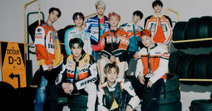 七位身穿賽車裝備的K-pop偶像，與輪胎和繞道標誌一起擺姿勢。 — Nct 127 壁紙
