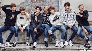 七個年輕男子身穿休閒服裝坐在混凝土階梯上對著鏡頭微笑 — BTS 壁紙