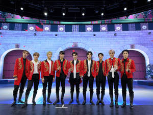 七名身穿紅色外套的表演者在城堡主題舞台上擺姿勢。 — Nct 127 壁紙