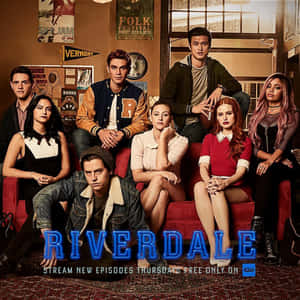 七名《Riverdale》青少年在裝飾有節目標題的房間裡的紅色沙發上擺姿勢。 — 河谷鎮 壁紙