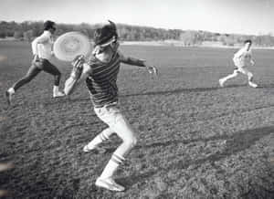 三人在草地上玩飛盤的黑白照片。 — 運動 壁紙