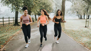 三位女性在秋天落葉滿地的公園小徑上一起慢跑。 — Running 壁紙