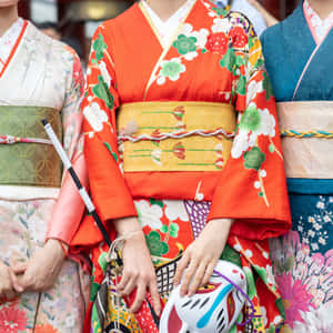 三位身穿彩色和服的女士在文化活動中手持裝飾面具。 — 日式粉紅 壁紙