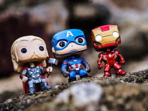 三個 Marvel 超級英雄動作人偶 Thor、Captain America 和 Iron Man 在岩石上擺姿勢。 — 鋼鐵人標誌 壁紙