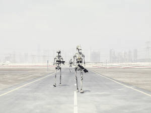 三個武裝機器人沿著塵土飛揚的高速公路走向遠方的城市。 — 機器人 壁紙