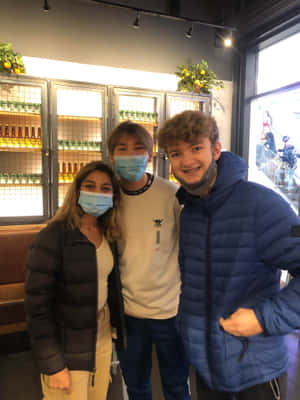 三個戴著口罩的朋友在一間酒吧裡擺姿勢，後面有啤酒架。 — 湯米英尼特 壁紙