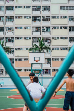 三個男孩在一棟高層公寓大樓前的戶外球場打籃球。