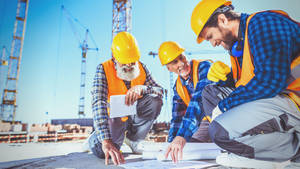 三名建築工人在陽光明媚的建築工地上審查藍圖。 — 工作 壁紙