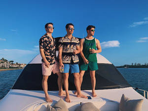 三名身穿夏威夷襯衫的男子在遊艇上享受日落時分的飲品。 — 強納斯兄弟 壁紙