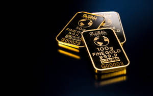 三塊金條，標有100g fine gold 999.9，放在深色反光表面上。